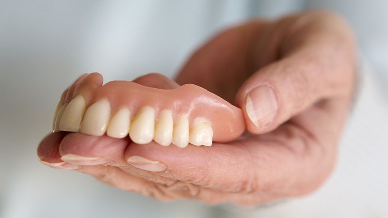 closeup of older womans hand holding a teeth denture